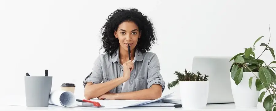 A person sitting at a work desk. She is holding a pen to their mouth.