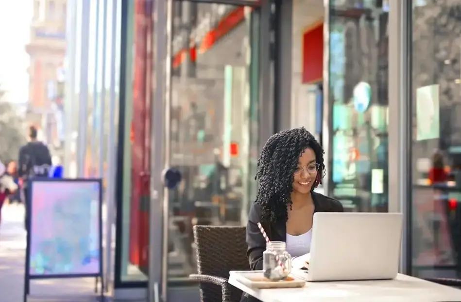 Imagem de uma moça sorrindo em frente de notebook sentada em uma mesa.