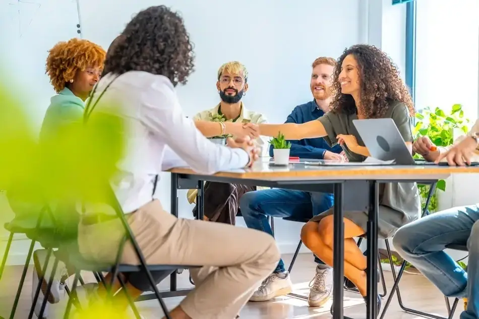 Foto de uma Equipe sentada em uma mesa se cumprimentando.