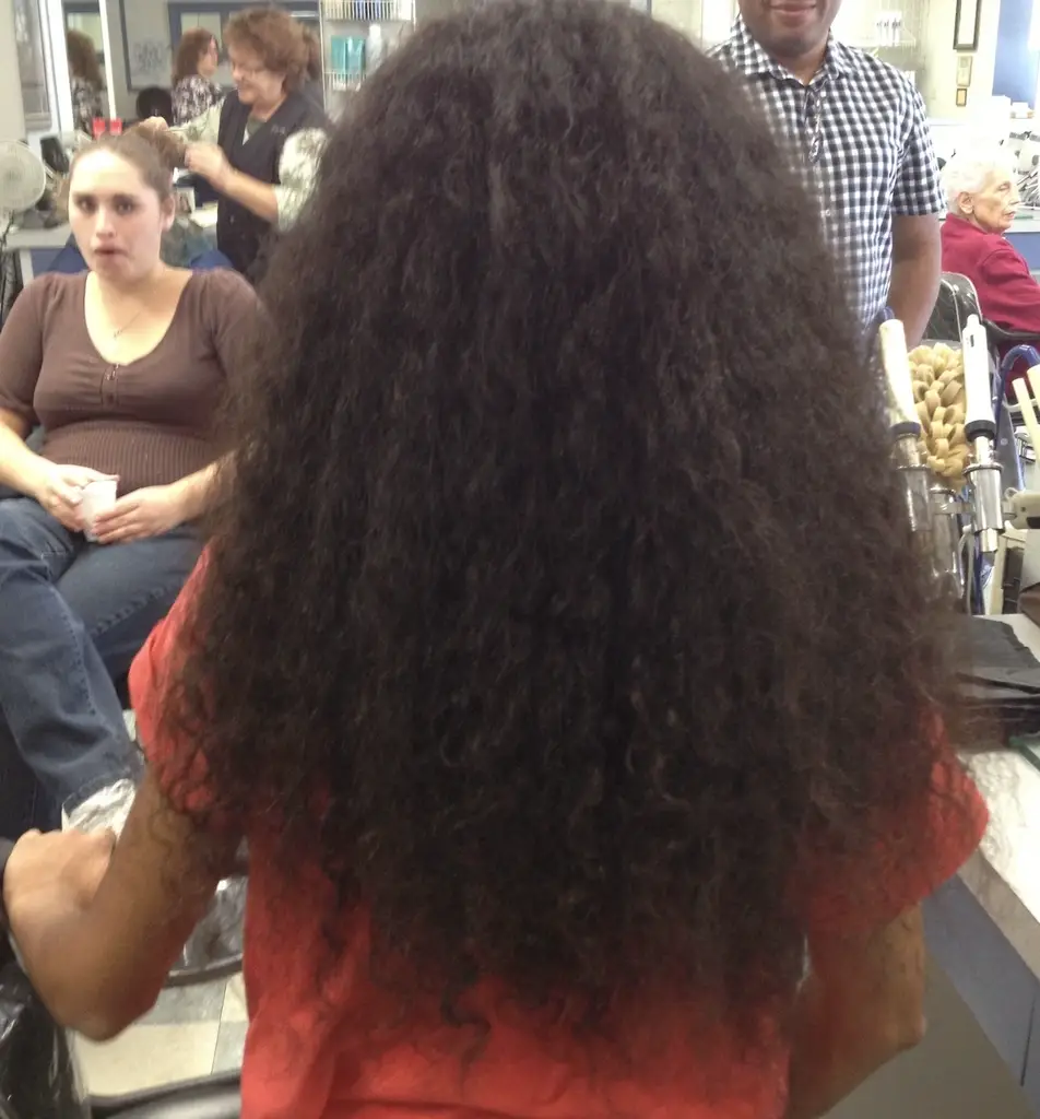 A photograph of a young girl sitting in a hair salon and preparing to donate hair to cancer patients.