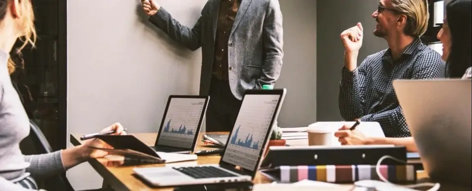 A group of people working in an office. One of them is standing by a board.