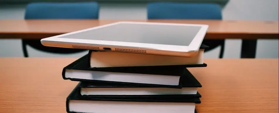 A pile of books with a tablet at the top of the pile.