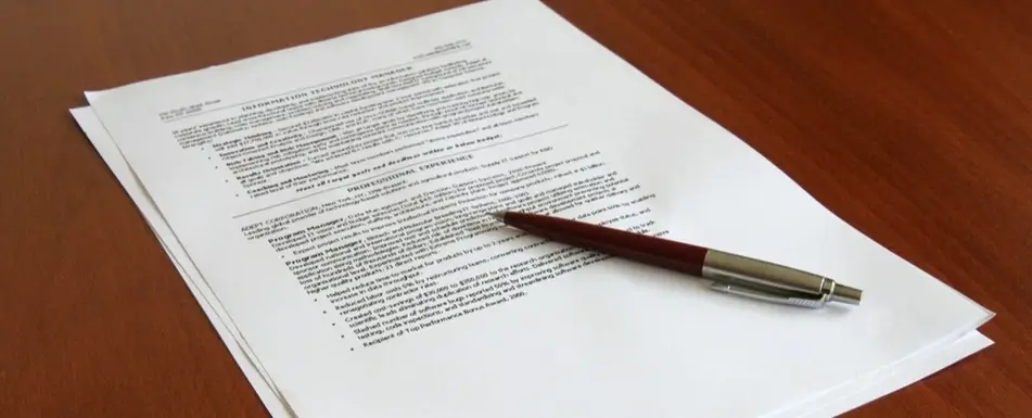 A printed resume and a pen on a table.