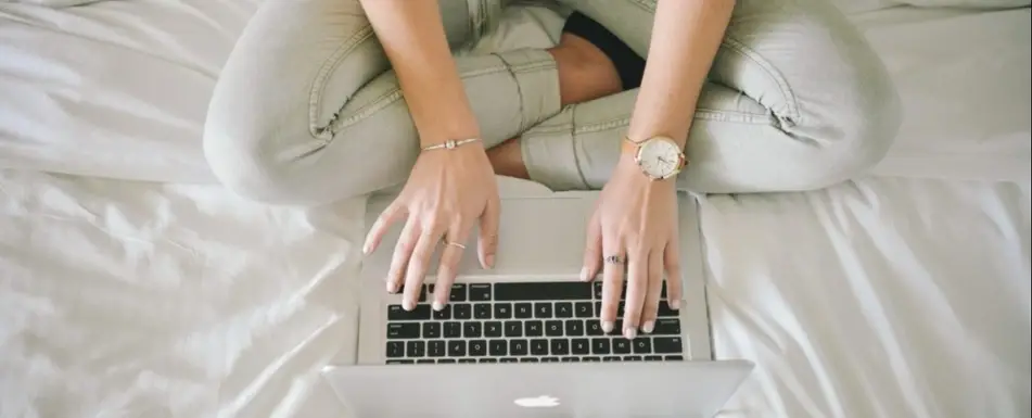 A person typing in bed on a laptop.