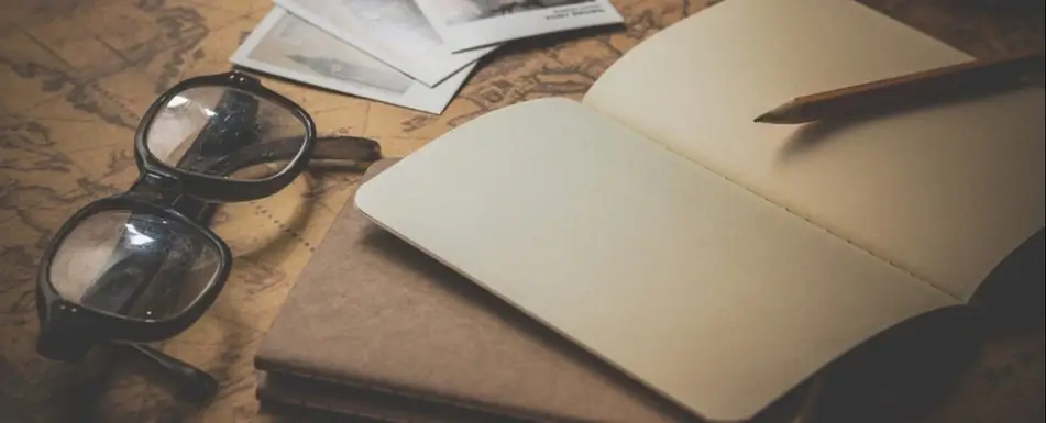 A table with a pair of glasses, book and a pencil.