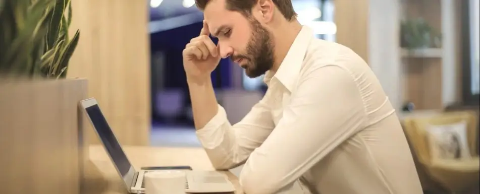 A man sits hunched over laptop at his desk.