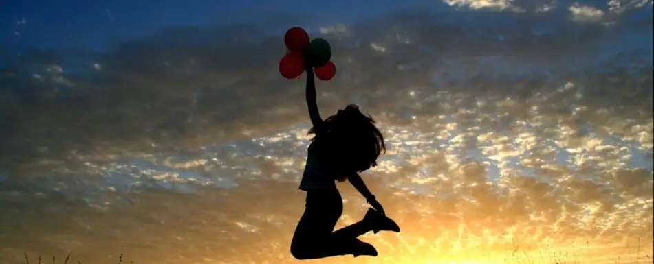 A woman with a fist full of balloons leaps towards the air.