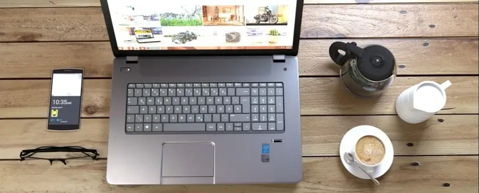 A desk with a laptop, smartphone, glasses and coffee.