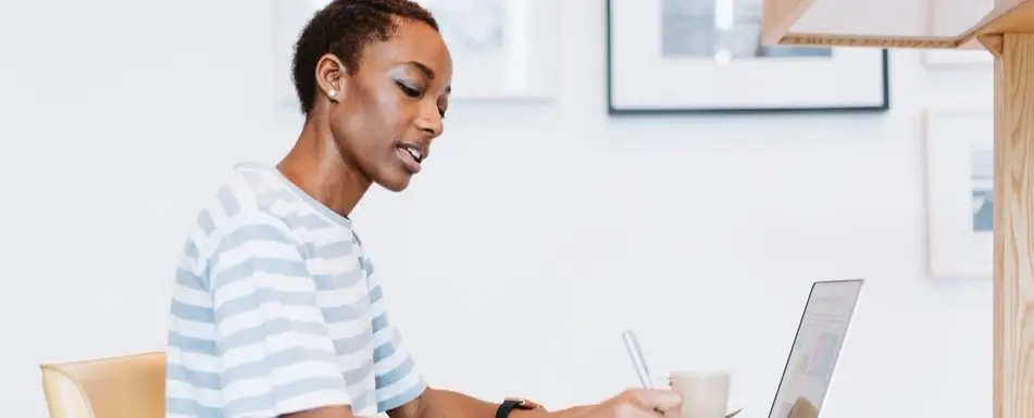 A person looking at their laptop and writing.