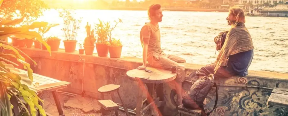 A couple sits by the water while the sun sets.