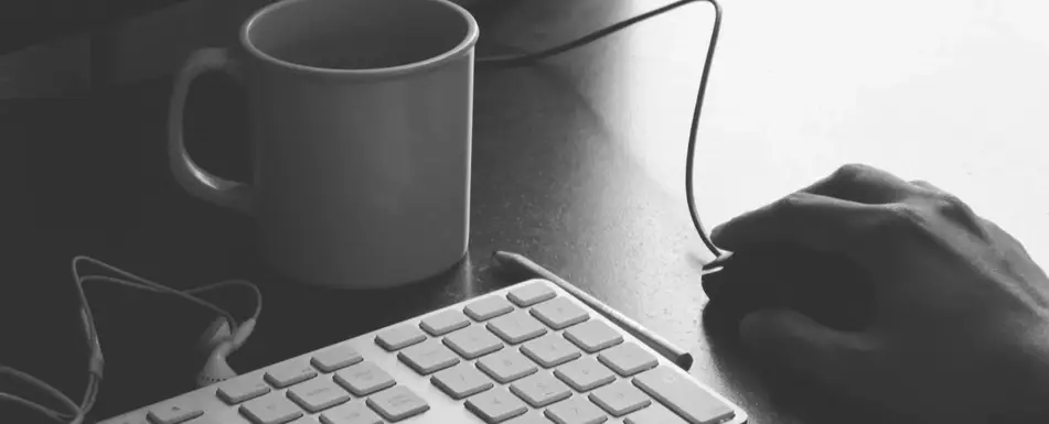 A person holding a computer mouse. On the table is also a keyboard and a mug.