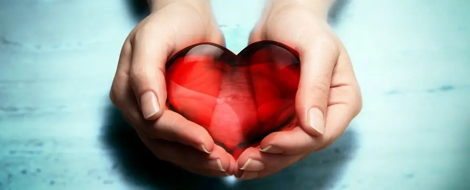 Two hands cupping a red glass heart.