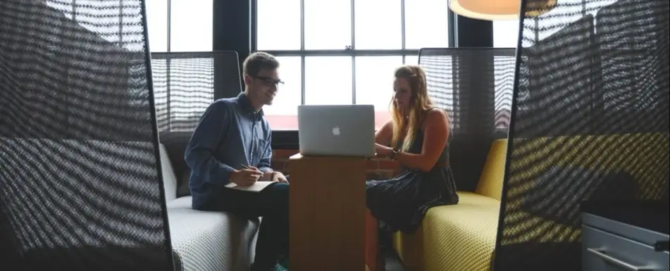 Two people sitting and looking at a laptop.