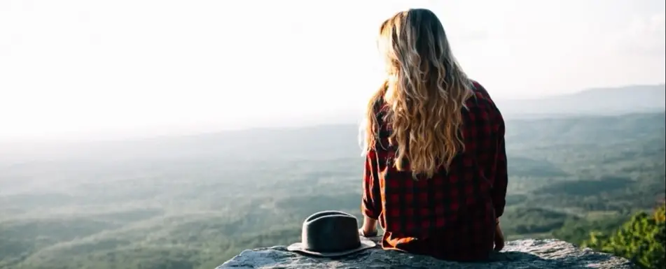 A person sitting on a cliff. Next to them is a hat.