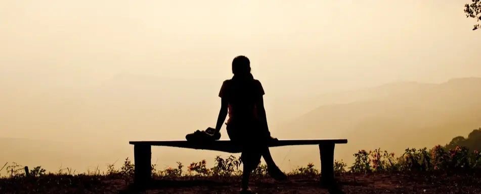 A woman sits at the edge of a mountain looking at the sunrise.