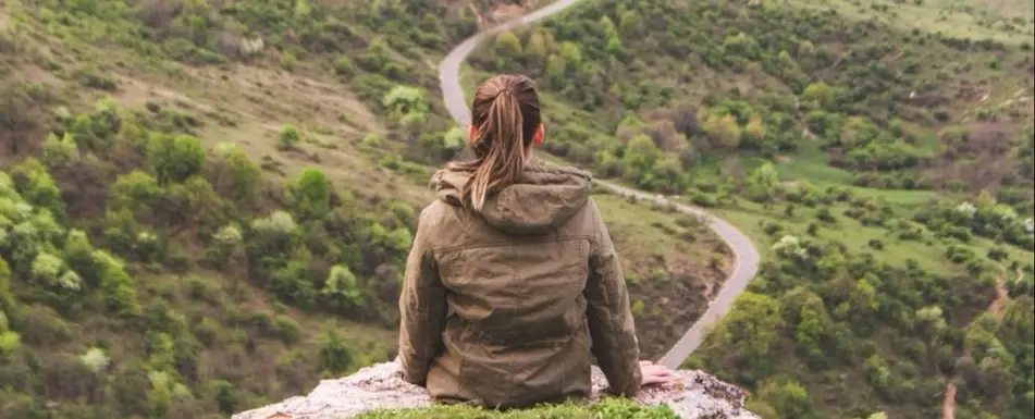 A person sitting on a cliff overlooking a forest.