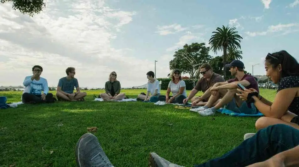 Círculo de personas sentadas en el pasto.