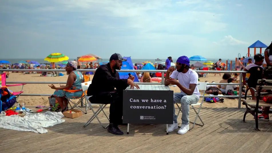 two people sitting at a table on a boardwalk with a sign that reads "can we have a conversation?"