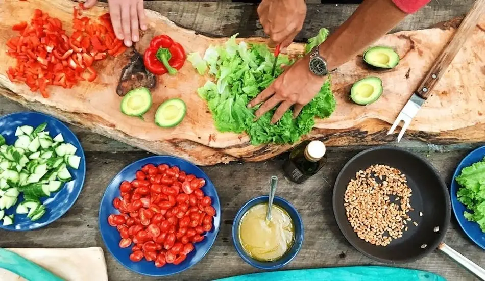 Grupo de personas cocinando sobre una tabla llena de ingredientes.