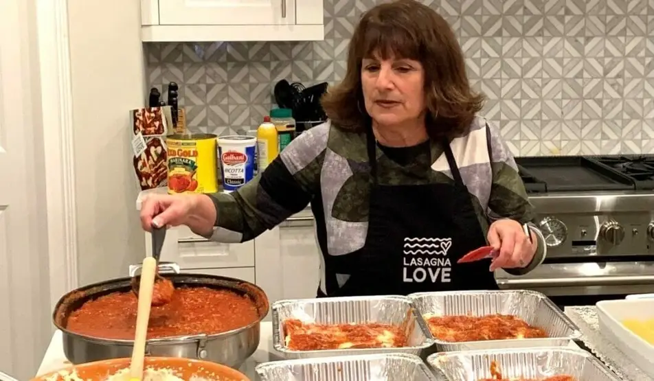 person wearing apron preparing trays of lasagna