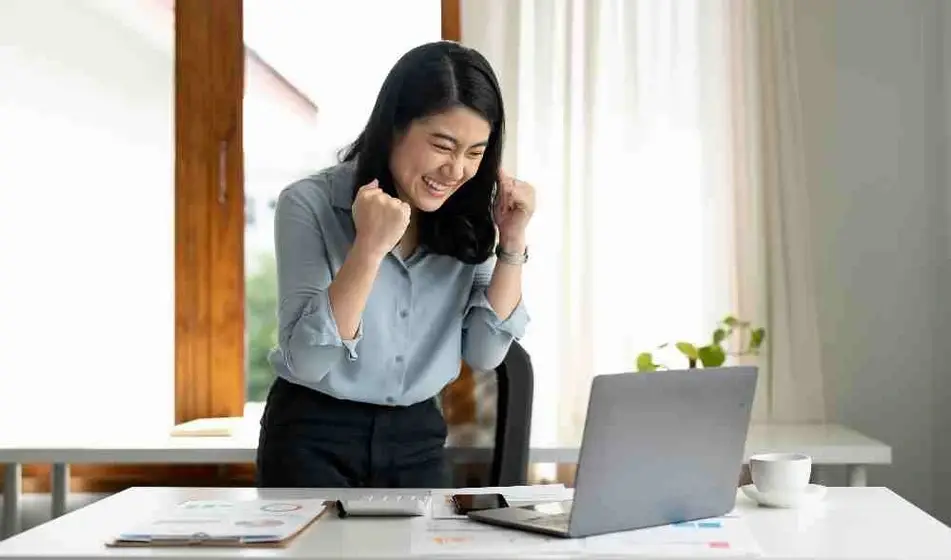 Mujer celebra un triunfo frente a su computadora.