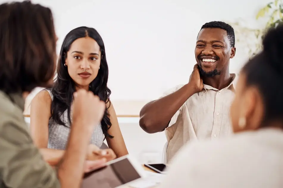 Co-workers talk at the lunch table collaborating on social change; Black man smiling at one co-workers as they speak.