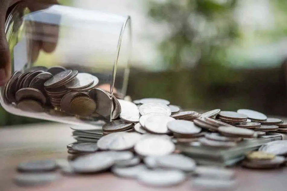 Una mano vierte monedas de un vaso de vidrio