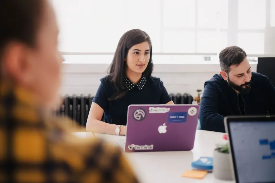 woman working at meeting table with colleagues and laptop