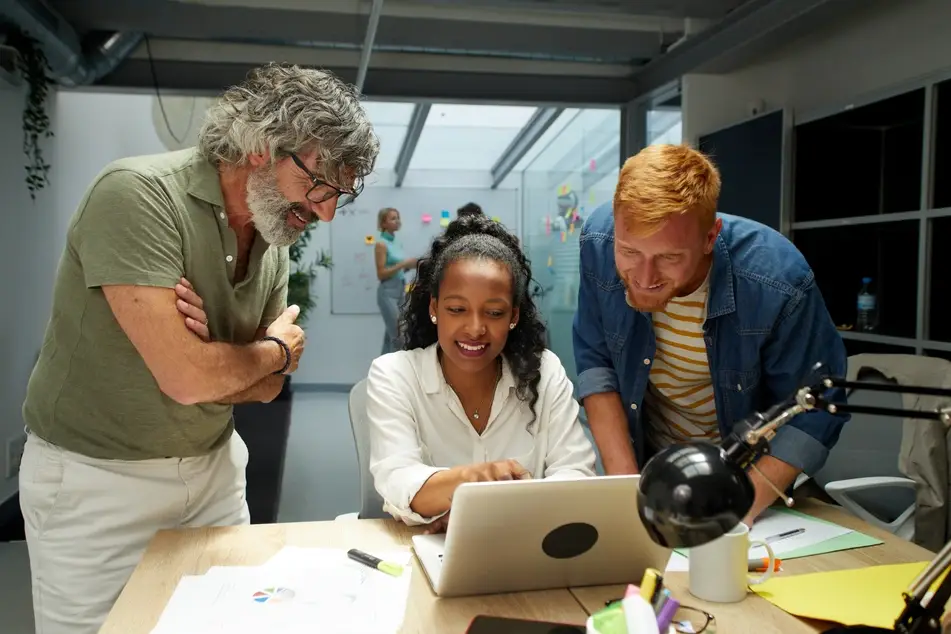 Multiracial colleagues gather around a laptop on a desk planning at a nonprofit.