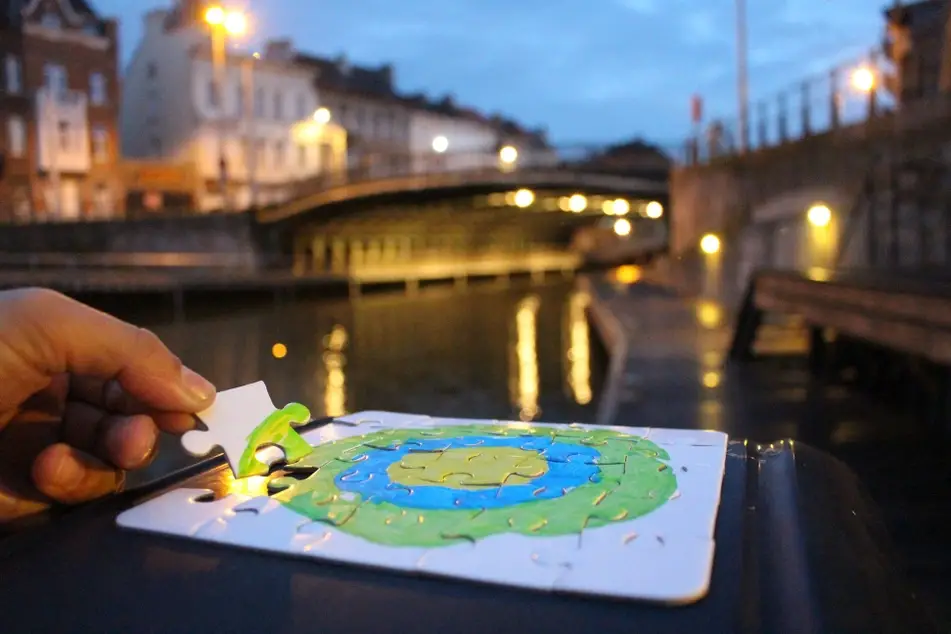 Someone plays a puzzle with the Idealist green, blue, and yellow logo on it while sitting on a riverbank in Belgium.