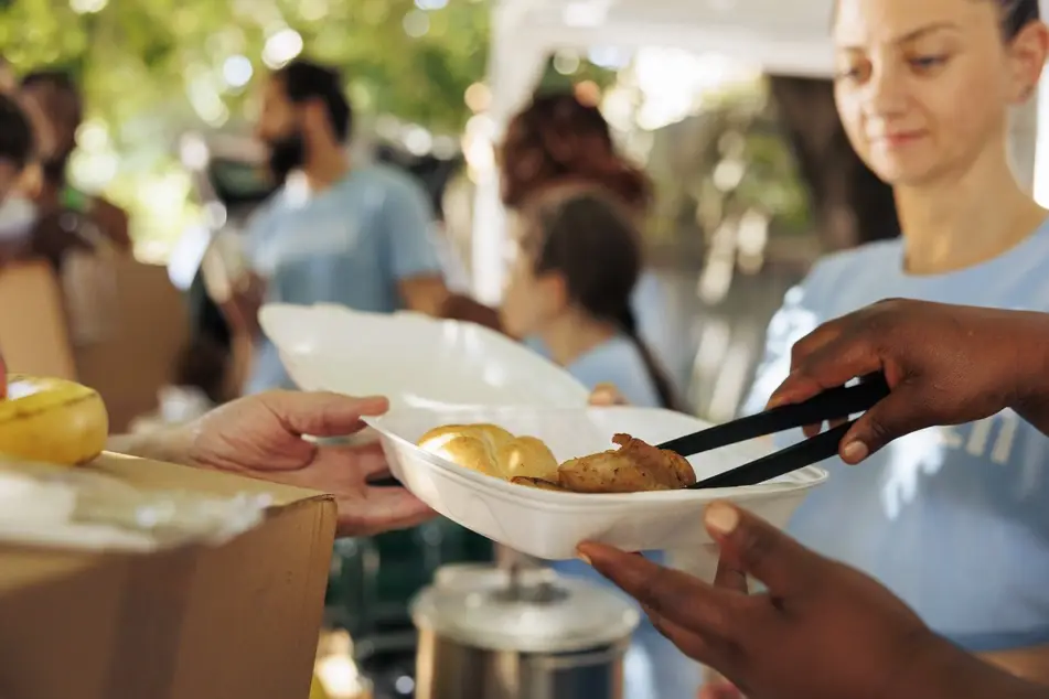 A group of volunteers wearing light blue t-shirts serve meals in an effort to address food insecurity and hunger.