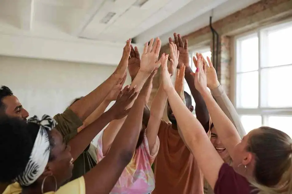 Equipo de personas reunidas alzando y juntando las manos.