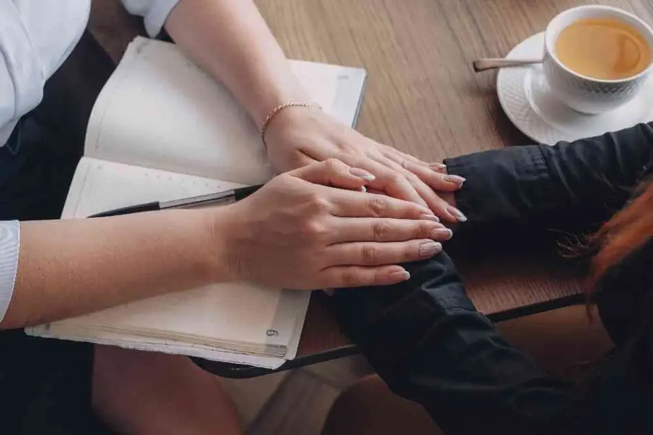 Dos mujeres con las manos juntas en señal de apoyo sobre una libreta abierta.