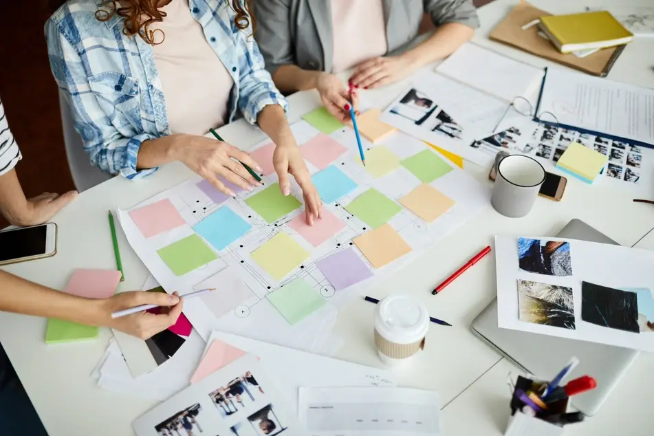 Several co-workers sit at a long office table planning their professional goals with post-it nots.