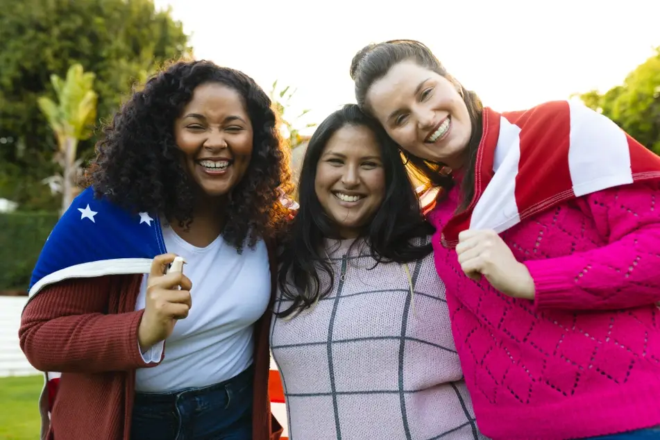 Three women of Latinx and Hispanic heritage smile while wrapped in an American flag.