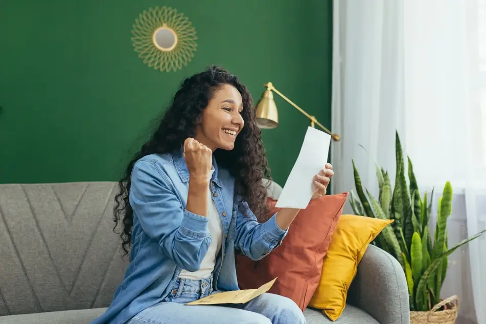 Girl with long dark, curly hair celebrates a grad school acceptance letter on her couch at home.