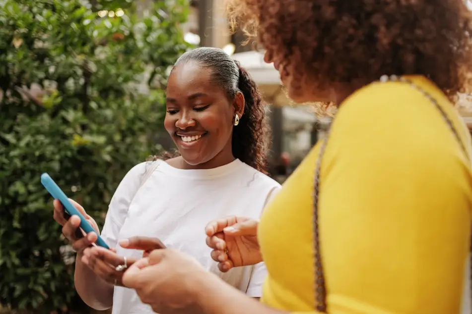 Two Black women talk outside, exchanging contact information as they network at a career event.