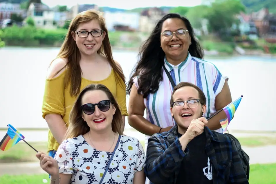 Group of friends standing outside waving LGBTQ+ Pride flags.