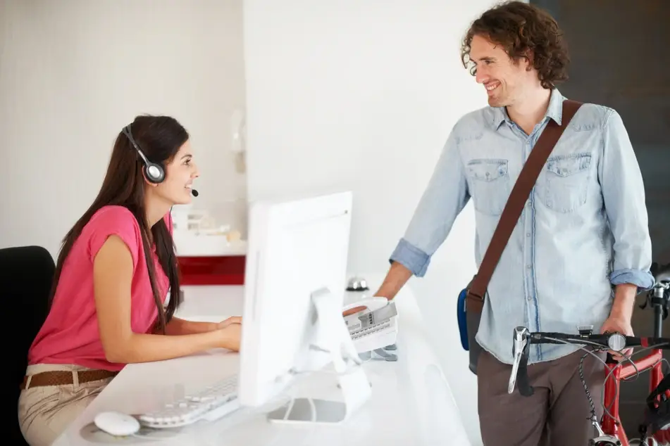 Woman in pink shirt working at a desk greets a bike messenger at office