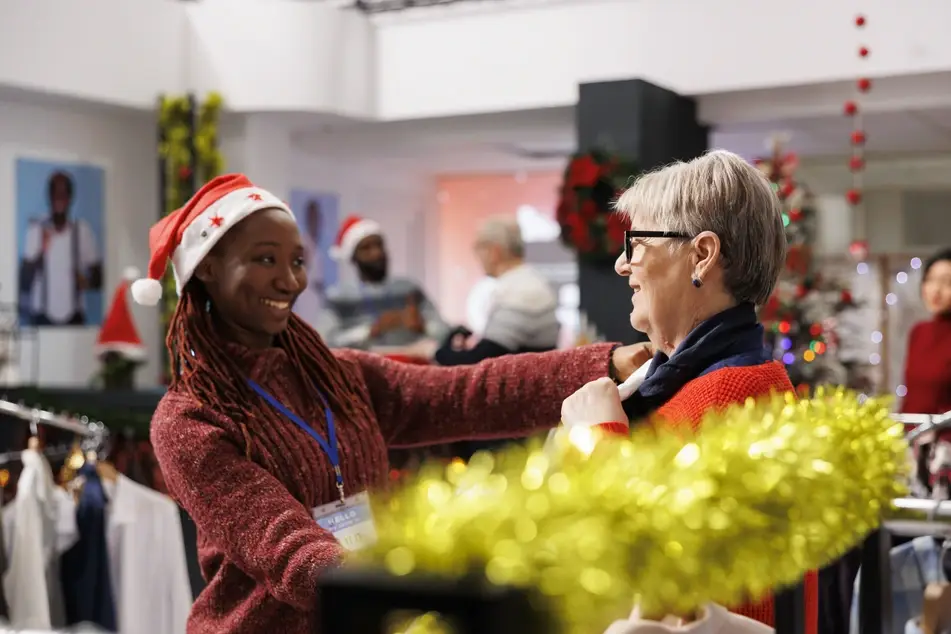 Young Black woman volunteers at a free store helping people find clothing during holiday volunteering.