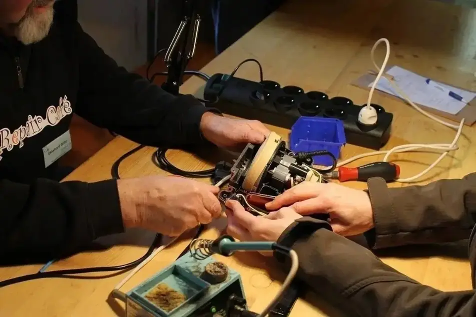 Dos personas trabajan en una mesa para reparar una pieza rota.