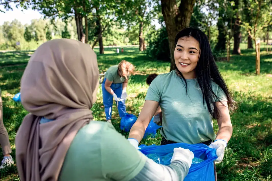 Two volunteers smile at each other while cleaning up trash outside with their mutual aid group.