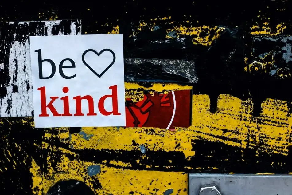 Adesivo escrito "be kind"com a figura de um coração em uma parede artística.