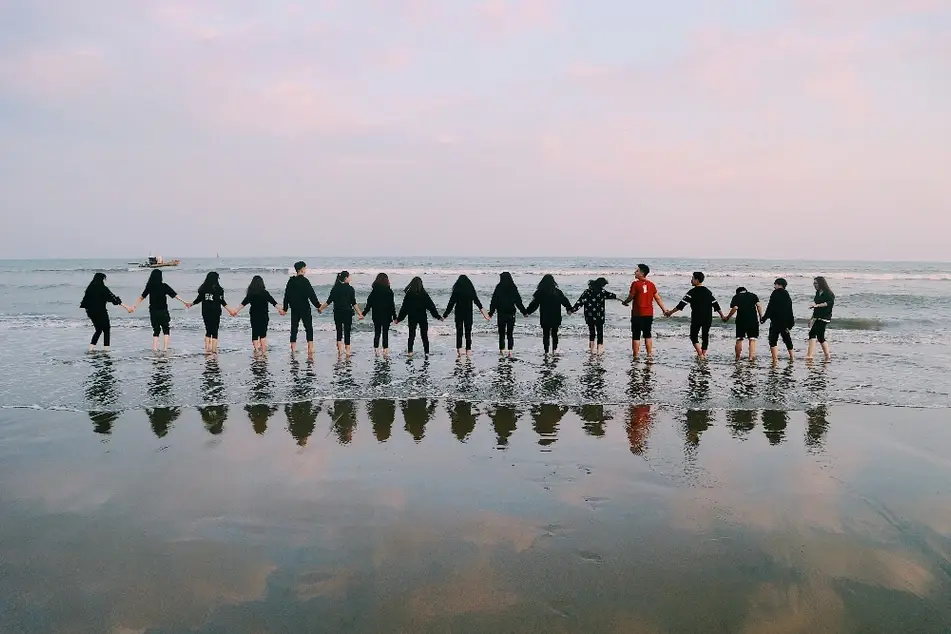 Grupo de personas tomándose de la mano a la orilla del mar