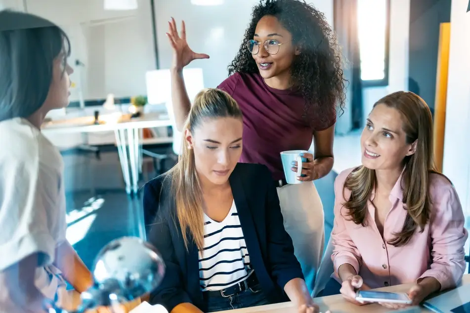 Four multiracial women sit in office discussing nonprofit fundraising and development  topics.