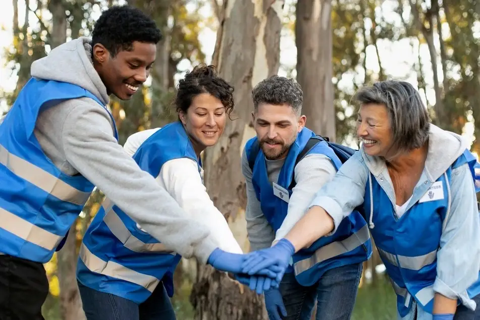 Imagem de 5 voluntários com coletes azuis unidos com as mãos juntas.