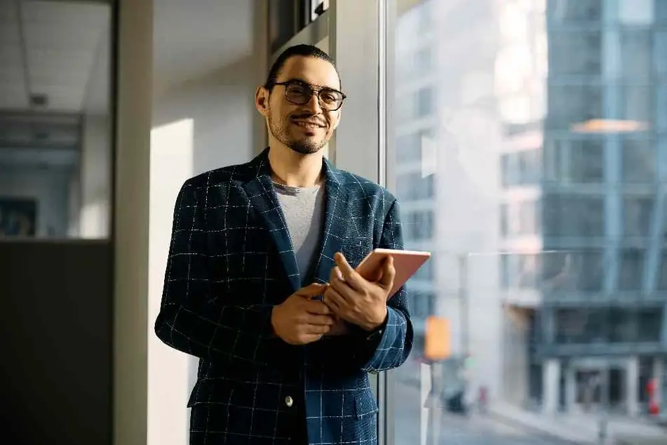 Hombre con traje y una tablet en la mano sonriendo a la cámara.