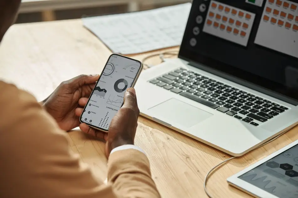 Two Black hands hold an iPhone while reviewing a productivity app at work.