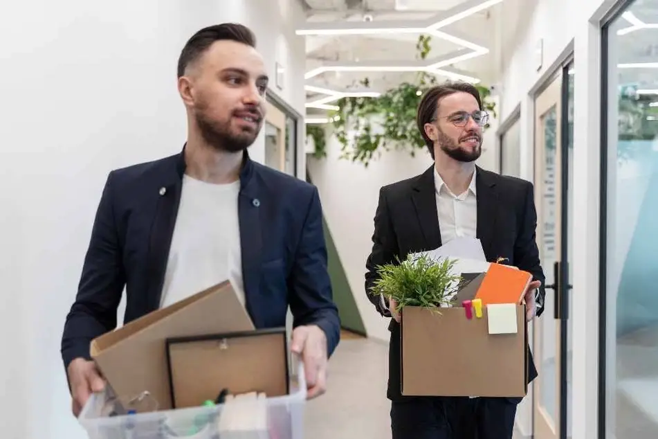 Dos hombres sosteniendo cajas con objetos personales dejando el trabajo