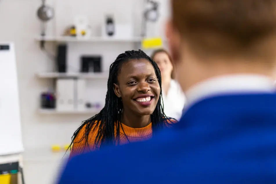 Black woman smiles at a man in blue suit in the middle of an office.